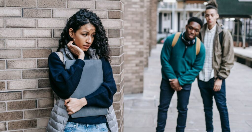 Socially awkward young woman leaning on a wall clutching a folder